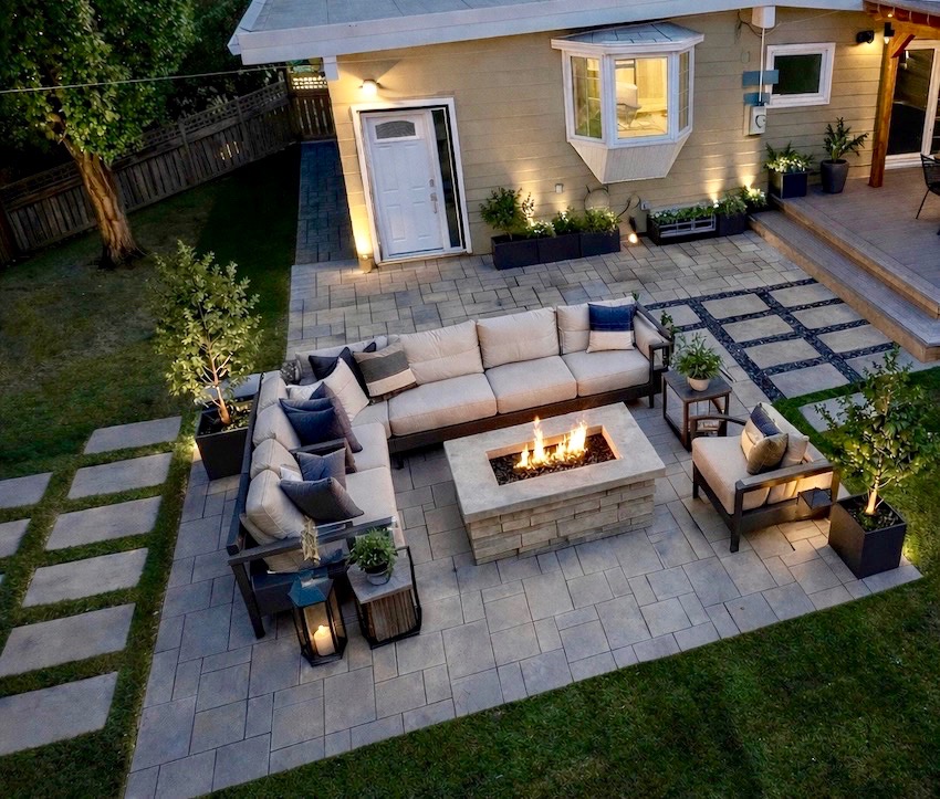 A custom Rundle Landscaping paving-stone patio at dusk with a lit fire feature and outdoor lounge furniture